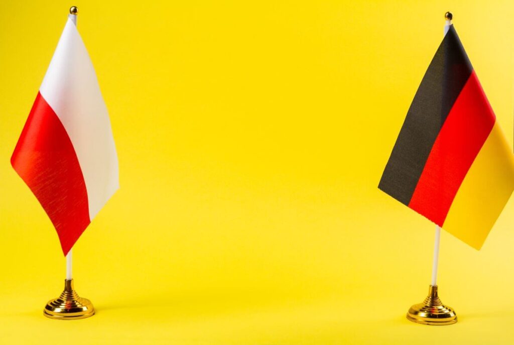 Na żółtym tle stoją obok siebie flagi Polski i Niemiec, symbolizując tłumaczenia z polskiego na niemiecki.