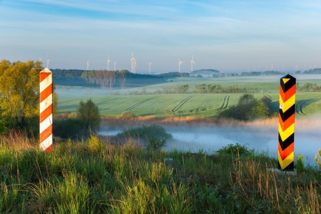 Słupki graniczne wśród pól i mgły symbolizują tłumaczenia z polskiego na niemiecki między sąsiadującymi krajami